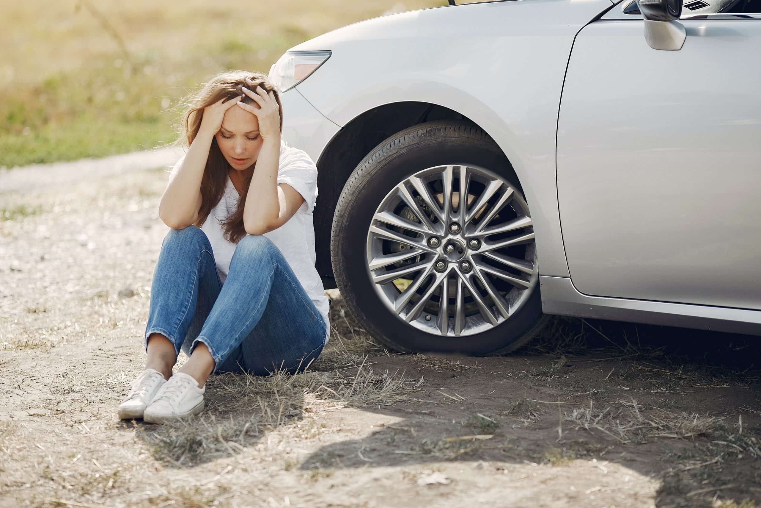 woman worrying while sitting near her broken car